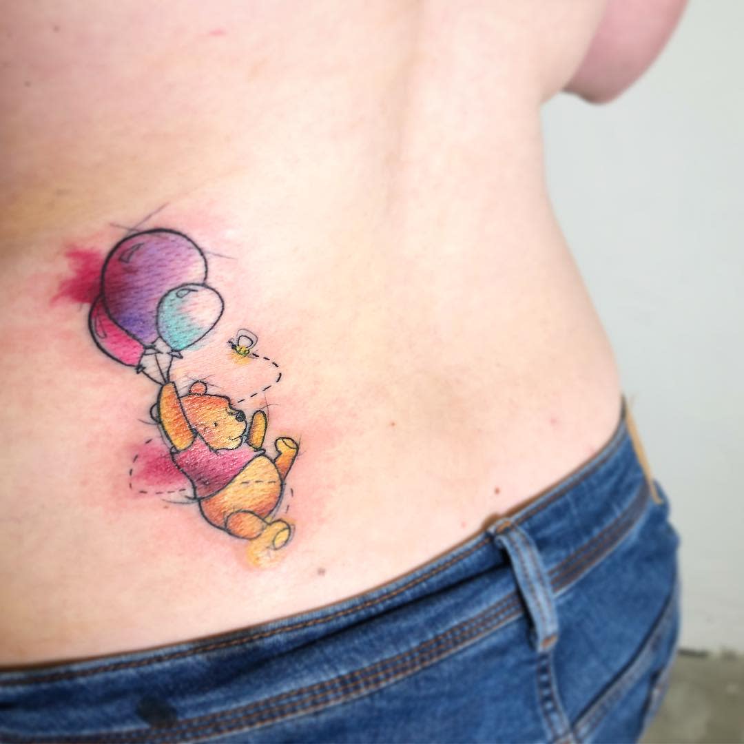 Watercolor tattoo of Winnie the Pooh holding onto balloons with a small bee flying around, located on the side of a person's torso